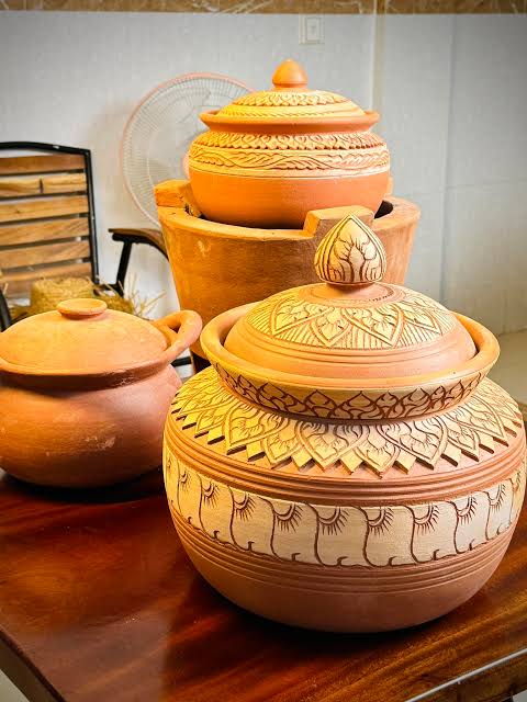 Three lidded earthenware pots stacked together on a wooden table.
