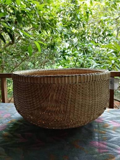An open-weave bamboo basket set on a table, photographed against trees.