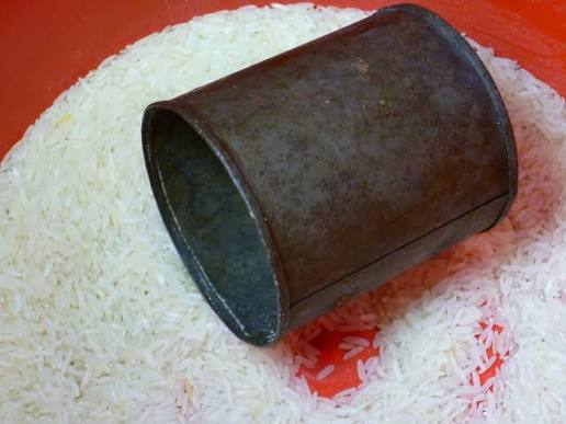 A dented condensed milk tin resting in a bowl of uncooked rice.