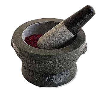 A stone mortar with the pestle leaning inside it and dried chili at the bottom.